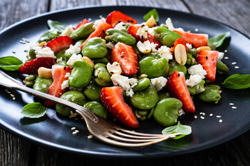Broad beans salad with feta cheese and strawberries on wooden table
