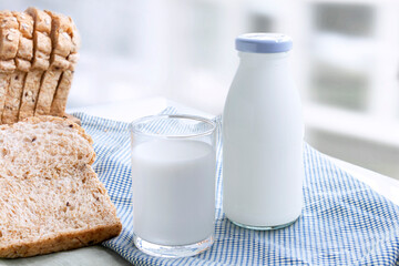 A bottle of milk and glass of milk with sliced bread on cloth indoors background for food and healthy concept.