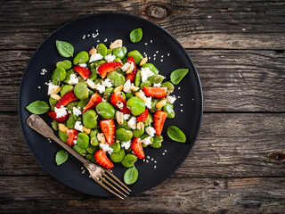 Broad beans salad with feta cheese and strawberries on wooden table
