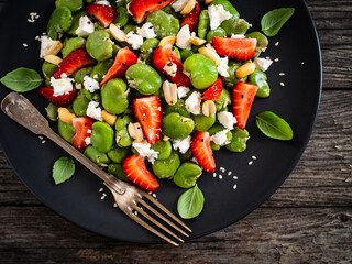 Broad beans salad with feta cheese and strawberries on wooden table
