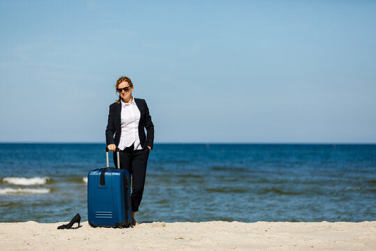 Woman with suitcase walking on beach
