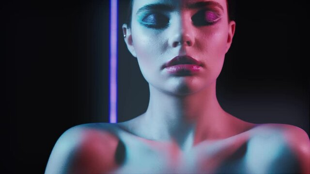Neon model portrait. Fashion art. Woman with bare shoulders and eyes closed posing in pink blue glow.