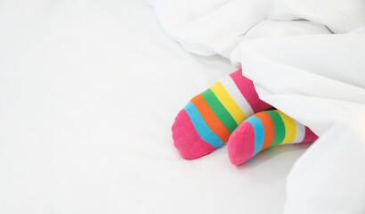 Female foot in warm stripe wool sock ,Woman sleeping and relaxing in bed concept. Warm and cozy white socks in the bed
