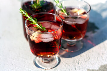 Two glasses and carafe with red refreshing summer drink or red wine, ice cube, pieces of watermelon and rosemary sprigs. Summertime concept. Selective focus.