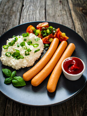 Breakfast - cottage cheese, boiled sausages and vegetables served on wooden table