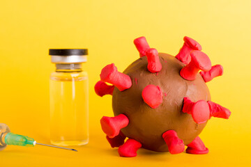 Closeup plasticine disease cells virus bottle vaccine and syringe of coronavirus outbreak and coronaviruses influenza flu, studio shot isolated on yellow background, pandemic COVID-19 medical health