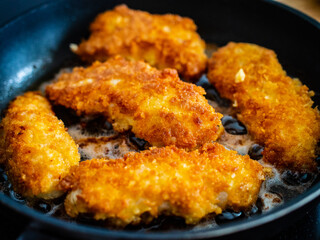Breaded chicken breast nuggets frying in pan