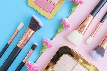 Obraz na płótnie Canvas premium makeup brushes, eye shadow palette and flowers on a colored blue and pink background, creative cosmetics flat lay with diagonal composition