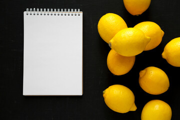 Ripe Yellow Organic Lemons and blank notepad on a black background, top view. Flat lay, overhead,...