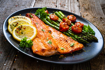Fried salmon fillet with asparagus and cherry tomatoes served on black plate on wooden table