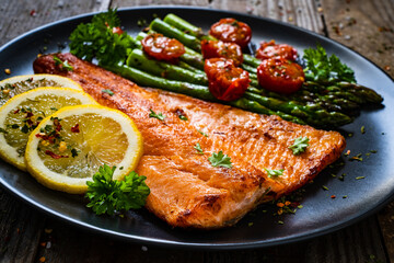 Fried salmon fillet with asparagus and cherry tomatoes served on black plate on wooden table