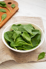 Fresh Baby Spinach in a white bowl on a white wooden table, side view.