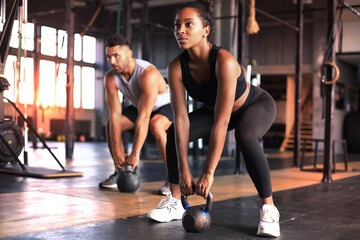 Fit and muscular couple focused on lifting a dumbbell during an exercise class in a gym.