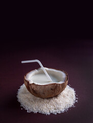 Cocos bowl with coconut milk into the nut at the heap of coco shavings isolated on dark background. Natural tropical fruit and drinks at minimalist style, close-up.