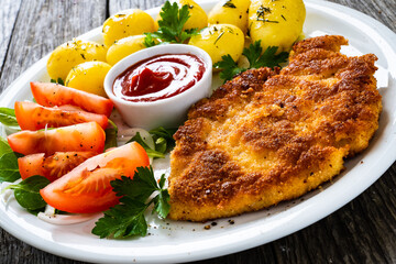 Breaded pork chop with boiled potatoes and vegetable salad on wooden background
