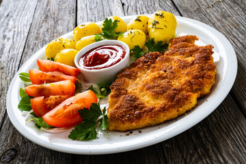 Breaded pork chop with boiled potatoes and vegetable salad on wooden background

