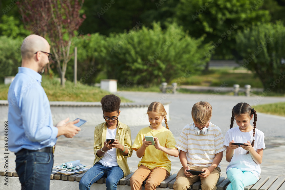 Canvas Prints multi-ethnic group of children using digital tablets while sitting in row on bench during outdoor le