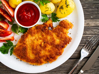 Breaded pork chop with boiled potatoes and vegetable salad on wooden background
