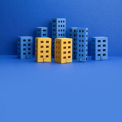 Miniature city with blue yellow paper houses on blue background. Abstract urban architecture landscape, simplified town layout with high-rise buildings, skyscrapers with many windows. copy space