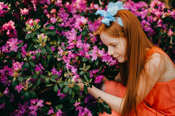 A cute girl in a summer dress enjoys plants in the botanical garden.