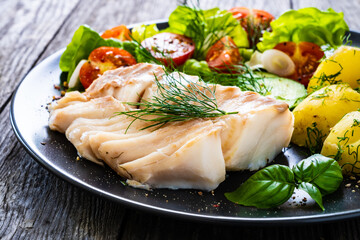 Fish dish - fried cod fillet with vegetables on wooden table
