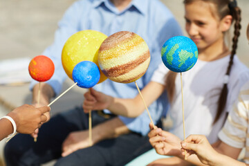 Close up of group of children holding model planets while enjoying outdoor astronomy lesson in sunlight, copy space