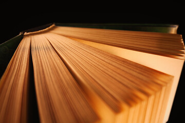 Obraz na płótnie Canvas Half open hardcover book in the dark with light softly illuminating book pages, view from above