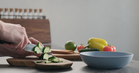 Obraz na płótnie Canvas Man chopping cucumber on olive wood board for greek salad
