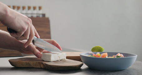 Man cutting feta cheese on olive wood board for greek salad