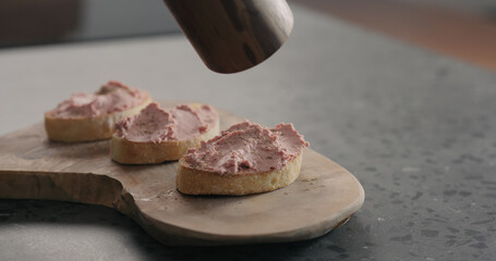 man grind fresh black pepper onto meat paste bruschettas on wood board