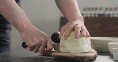 man chopping iceberg lettuce on wood board