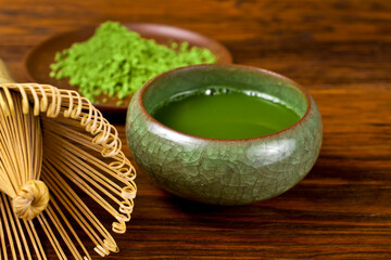 Green matcha tea in a cup with powdered matcha tea in a plate and bamboo matcha tea whisk also know as chasen on a wooden background. Selective focus.