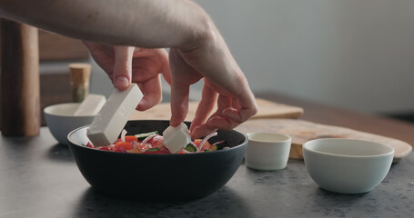 man put feta cheese into greek salad in black bowl