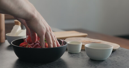 man mixing greek salad in black bowl with wood servers