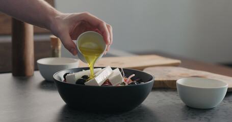 man pour olive oil over greek salad in black bowl