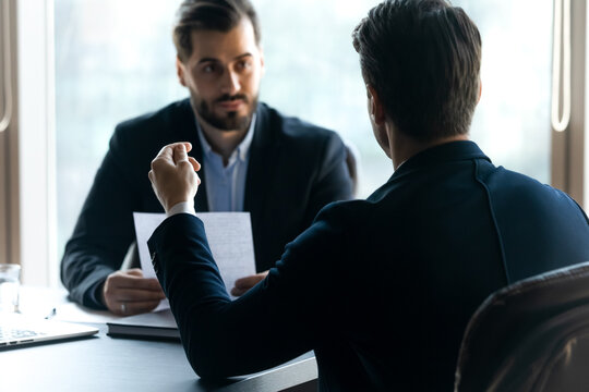 Back Rear View Young Motivated Man In Formal Wear Answering Questions Of Serious Interested Male Hr Manager, Sharing Experience Or Working Skills At Dream Job Interview In Modern Corporate Office.