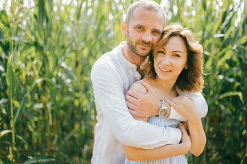 Fototapeta premium Attractive caucasian woman with short wavy dark hair in blue dress with her strong husband with short dark hair in white shirt and blue jeans relaxes together in the village cornfield