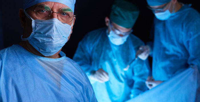 Group of surgeons at work in operating theater toned in blue. Medical team performing operation