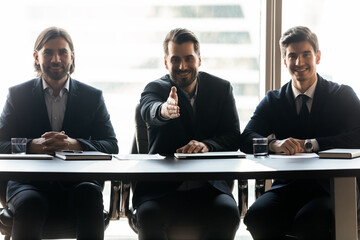 Smiling friendly young male hr managers in suits sitting at table, looking at camera, stretching...