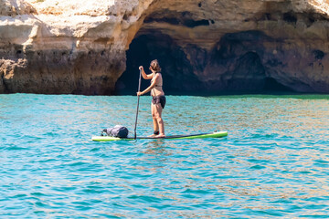 Woman paddle surfing in benagil caves over turquoise waters
