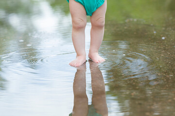 Baby legs standing in shallow puddle after warm rain. Front view. Barefoot closeup.