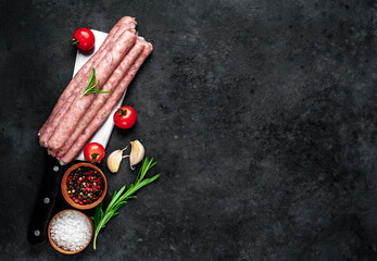 
Thin raw meat sausages over a meat knife on a stone background with copy space for your text