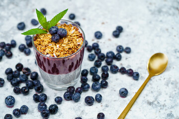 Healthy breakfast or morning snack with chia seeds pudding, granola, muesli and blueberries on white stone background, vegetarian food, diet and health concept.