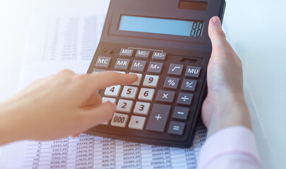 Financial data analyzing. Close-up photo of a businesswoman hand writing and counting on calculator in office. Selective focus