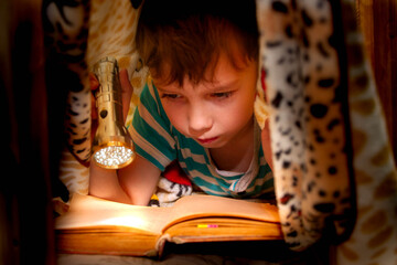 The child carefully reads the book by the light of a flashlight. Flashlight illuminates the text in...