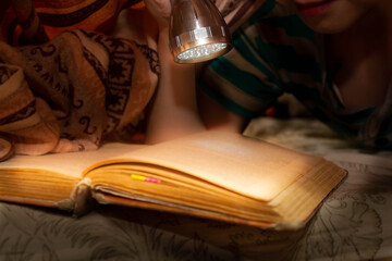 Shine a flashlight on a book in the dark under a blanket. Hiding under the covers with an...