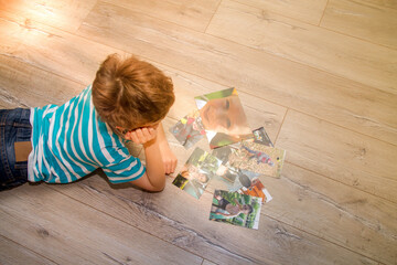 The boy lies on the floor in the apartment and looks at his printed on paper photos. The child...