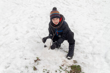 Fototapeta na wymiar A teenage boy sculpts a snowman out of snow in winter on the Playground at home. The child makes a lump of fresh white snow. Thaw.