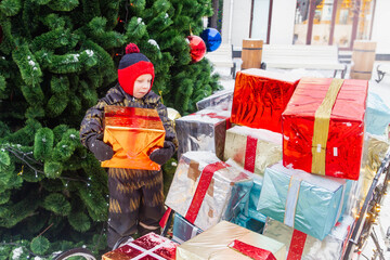 A European boy is holding a large box with a Christmas present and laughing. Outdoor. Winter. Snow. The child is happy.