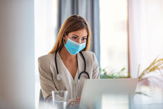 Female Healthcare Worker Counseling, Helping Patient Online In Her Office. Wearing Protection Mask During Corona Virus Outbreak. Mid Adult Female Doctor Working In Office.